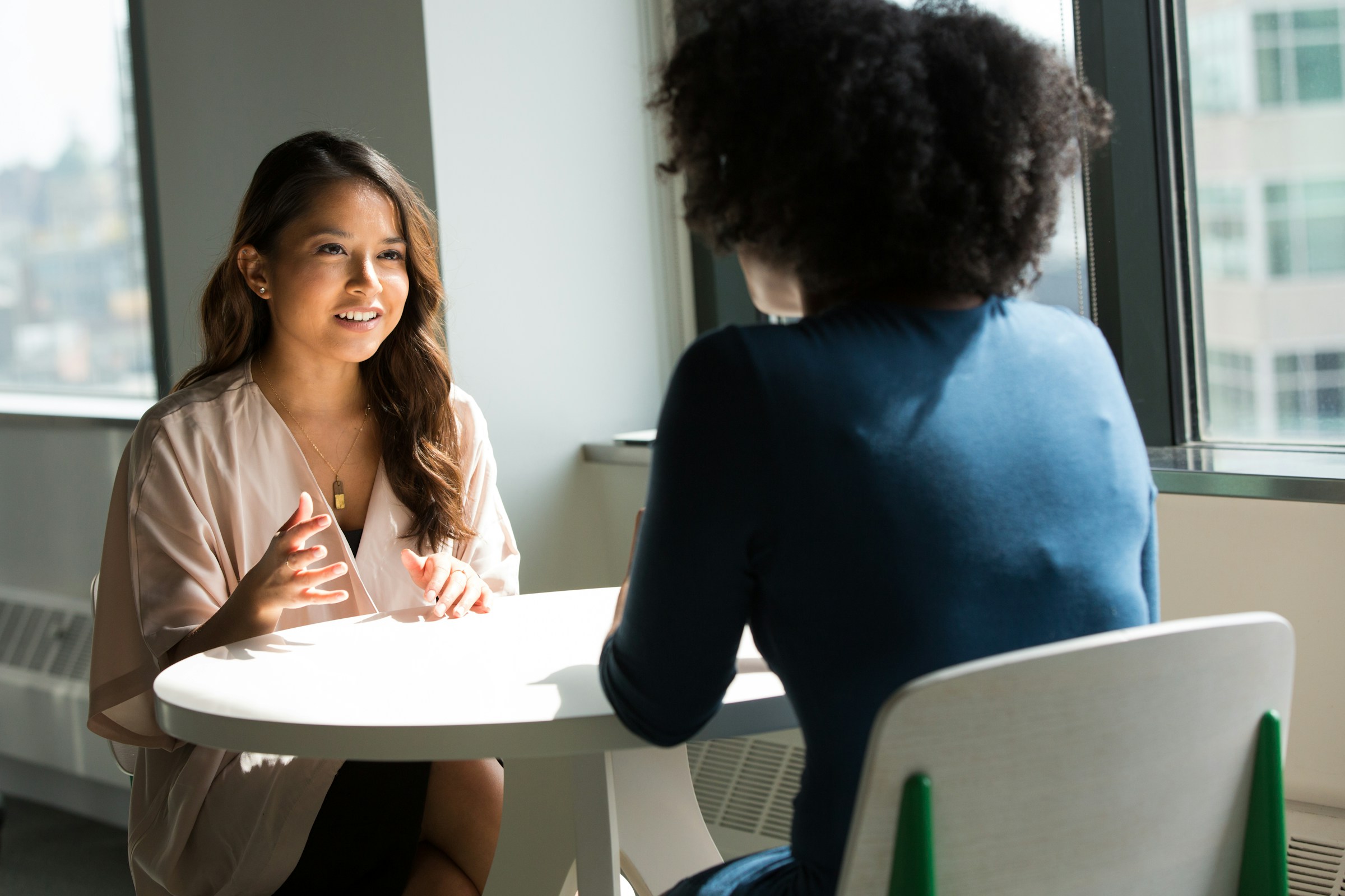 Two women in professional conversation at a round table - Anjali's Desk, Mindfield Resources.